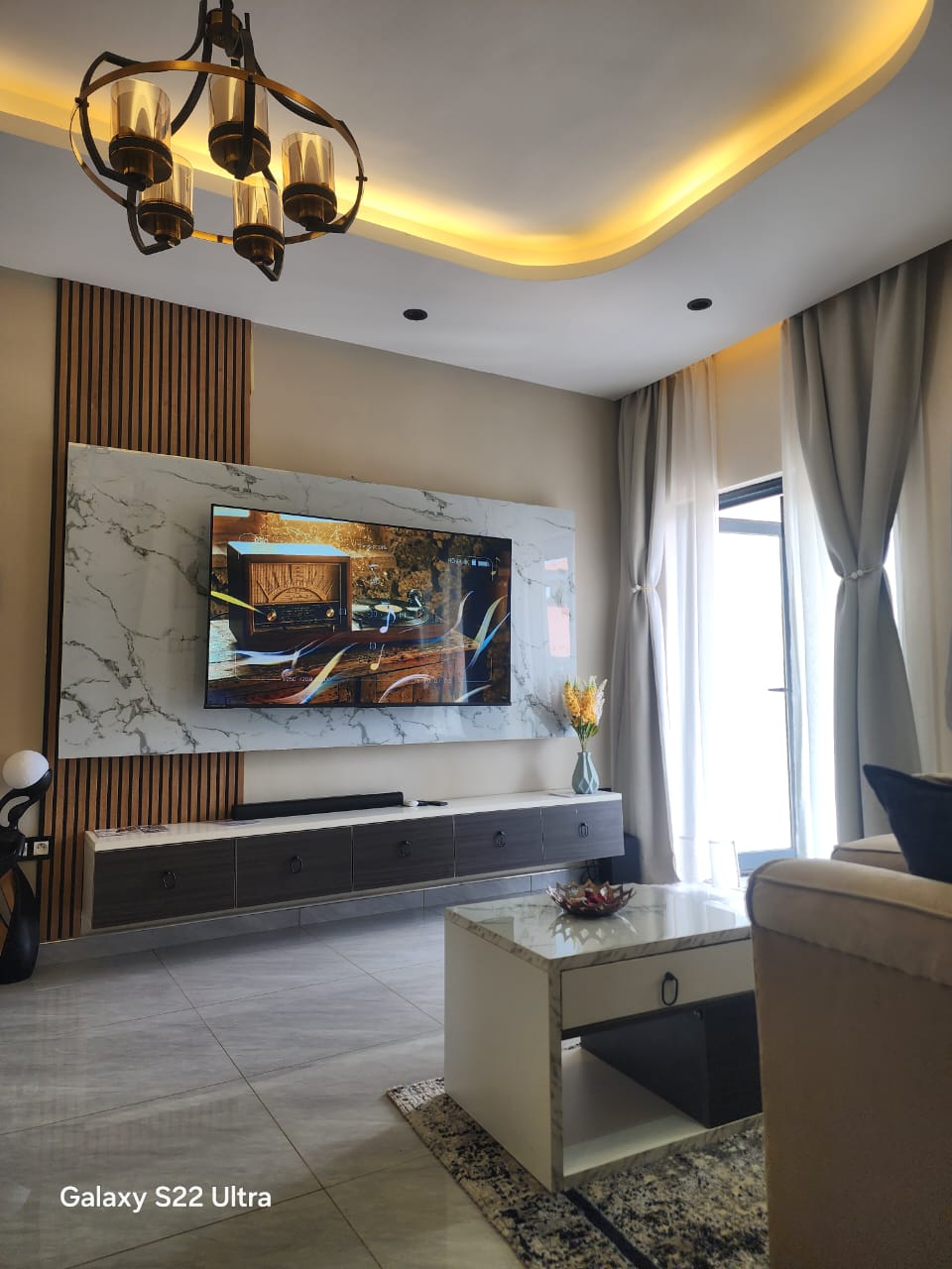 Living room with marble TV wall, wood slats and LED cove